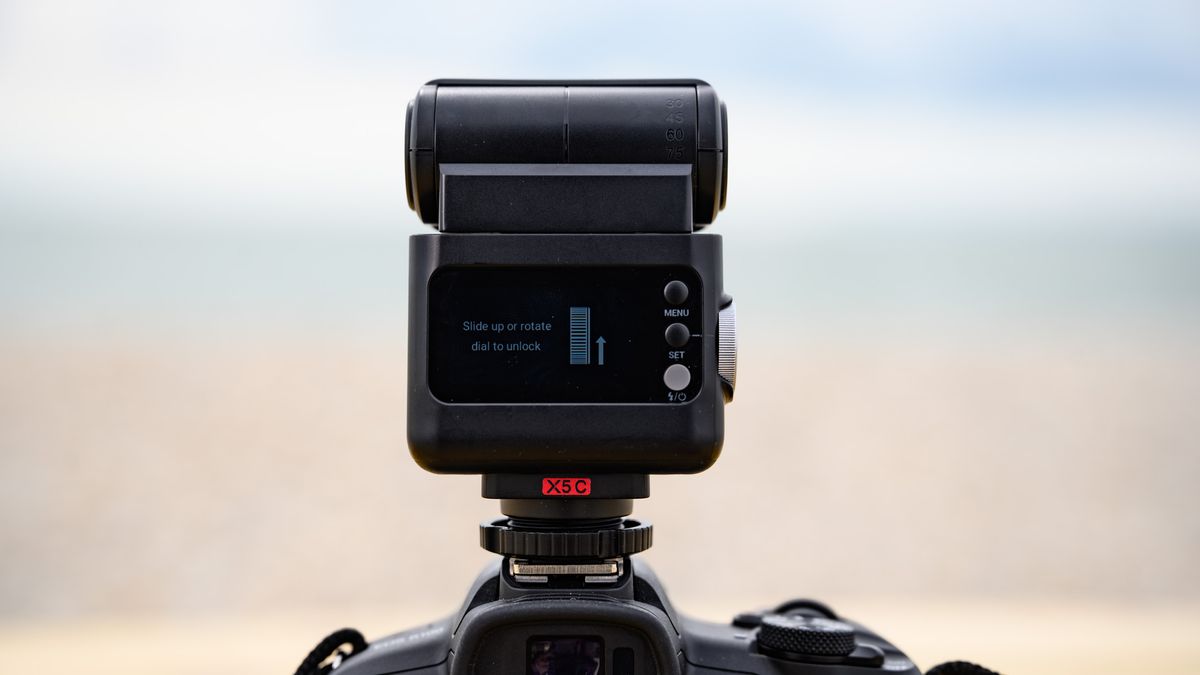 Closeup of the Godox iT32 camera flash and its rear display, the ocean is behind it