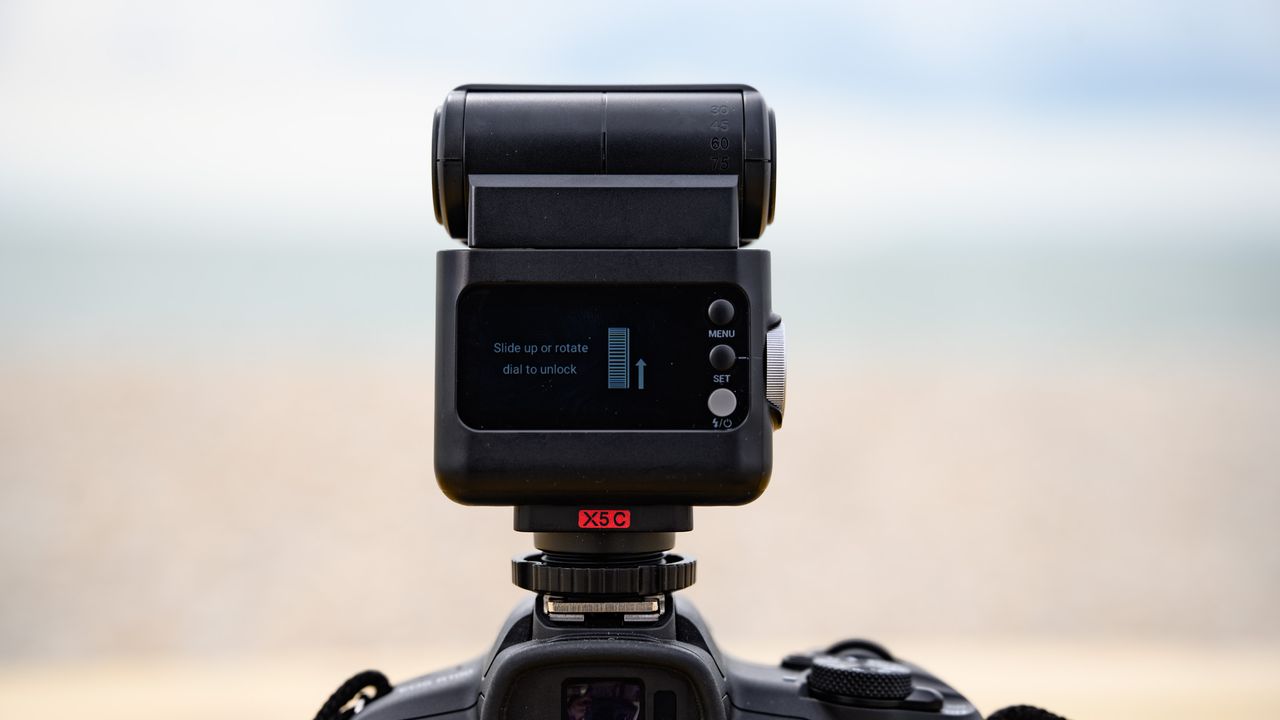 Closeup of the Godox iT32 camera flash and its rear display, the ocean is behind it