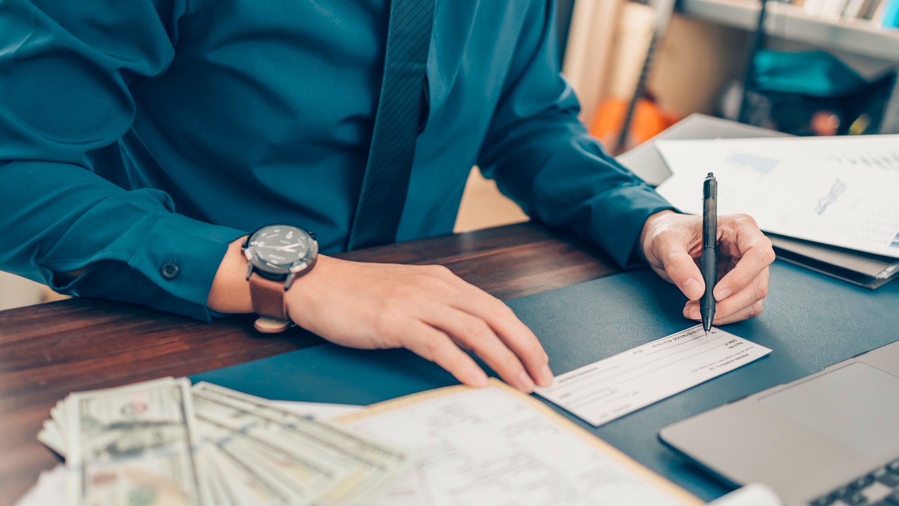 A young man at a desk starts filling in a check.