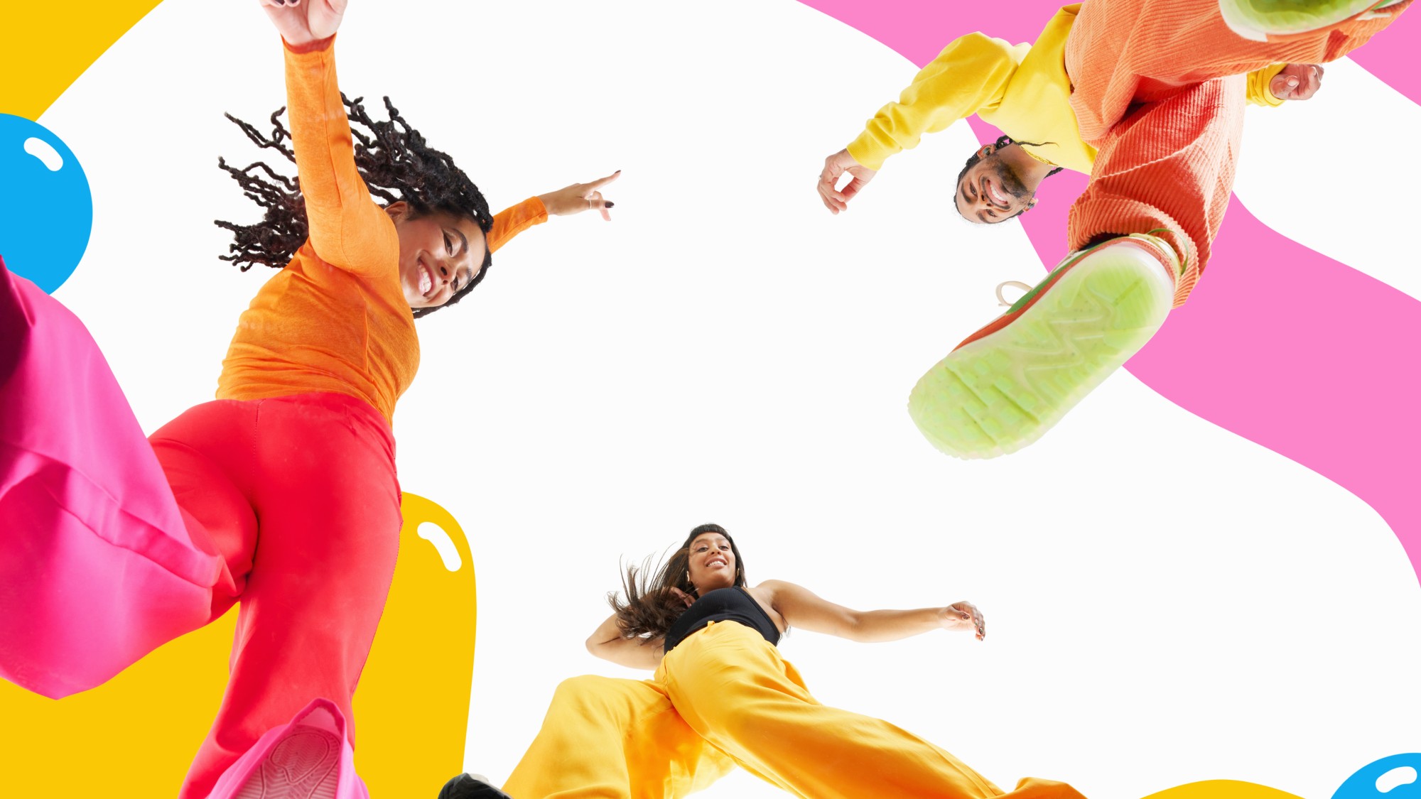full length studio shot of three people looking down at camera smiling and dancing against colourful background