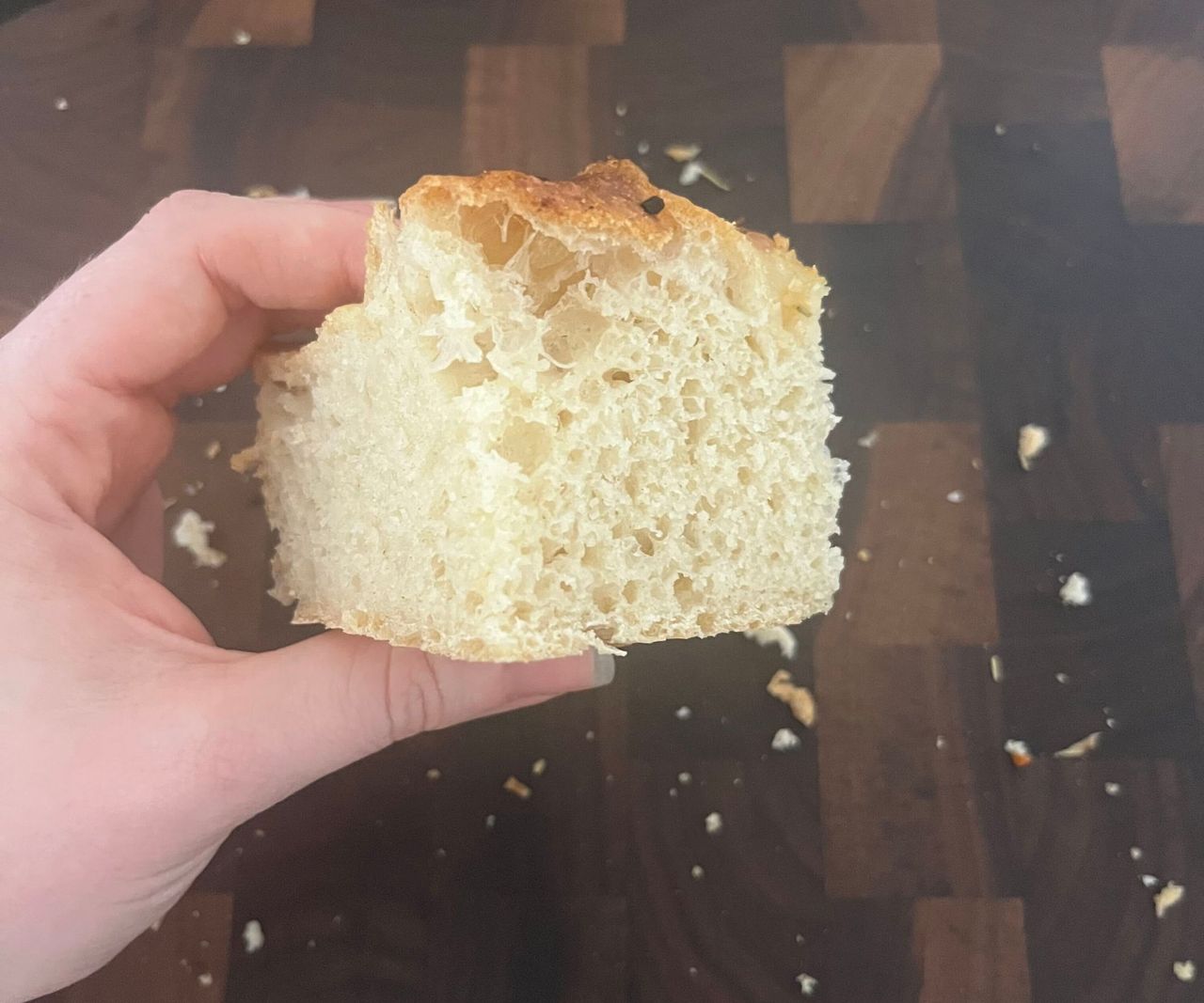 A cube of freshly cut focaccia bread being held above a wooden cutting board