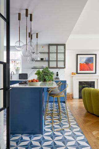 a blue kitchen with a split flooring of patterned tiles and wood parquet