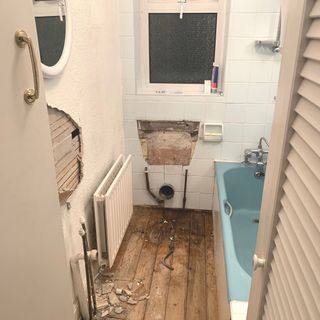 bathroom half way through renovtion with blue bath and wooden floor exposed