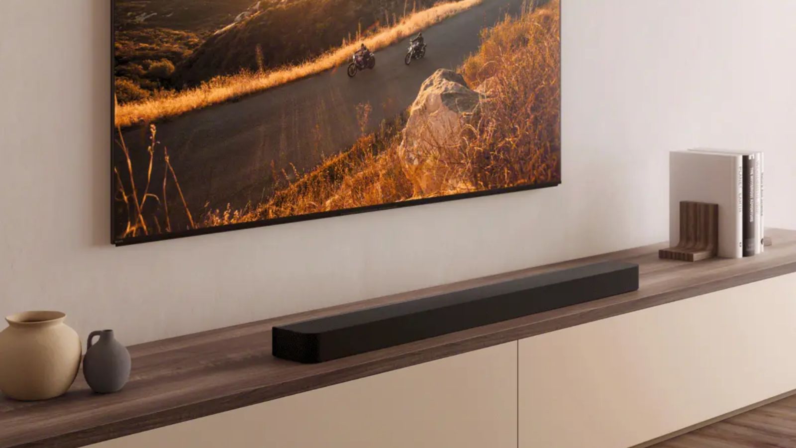 Sony BRAVIA Theater Bar 8 soundbar on wide TV stand below large TV showing a nature scene, next to ceramic pots and books.