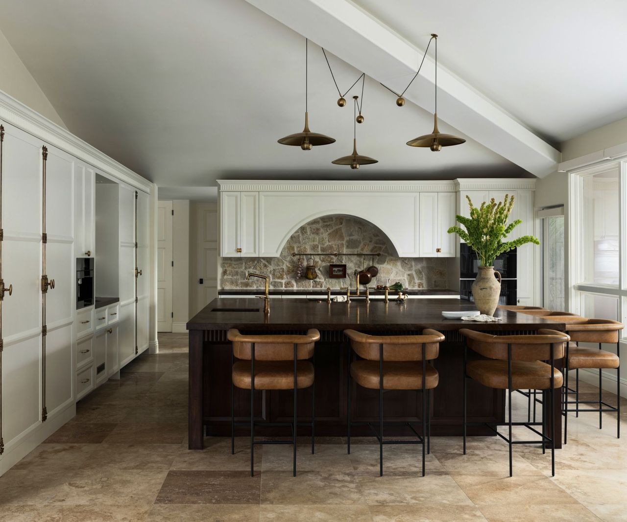A wood and white kitchen with a dark wood kitchen island, white cabinetry, and brass hardware