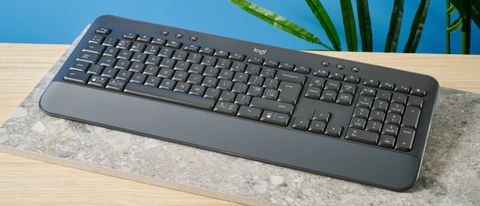 a black full sized keyboard with batteries and a palm rest on a clean beige surface with a blue backdrop