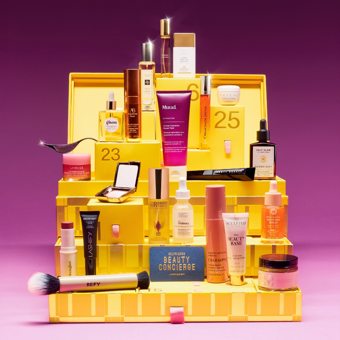 The yellow Selfridges Beauty Advent Calendar 2025 with its contents stacked on top, on a purple background