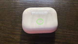 A green circle highlights the button on the back of the AirPods case