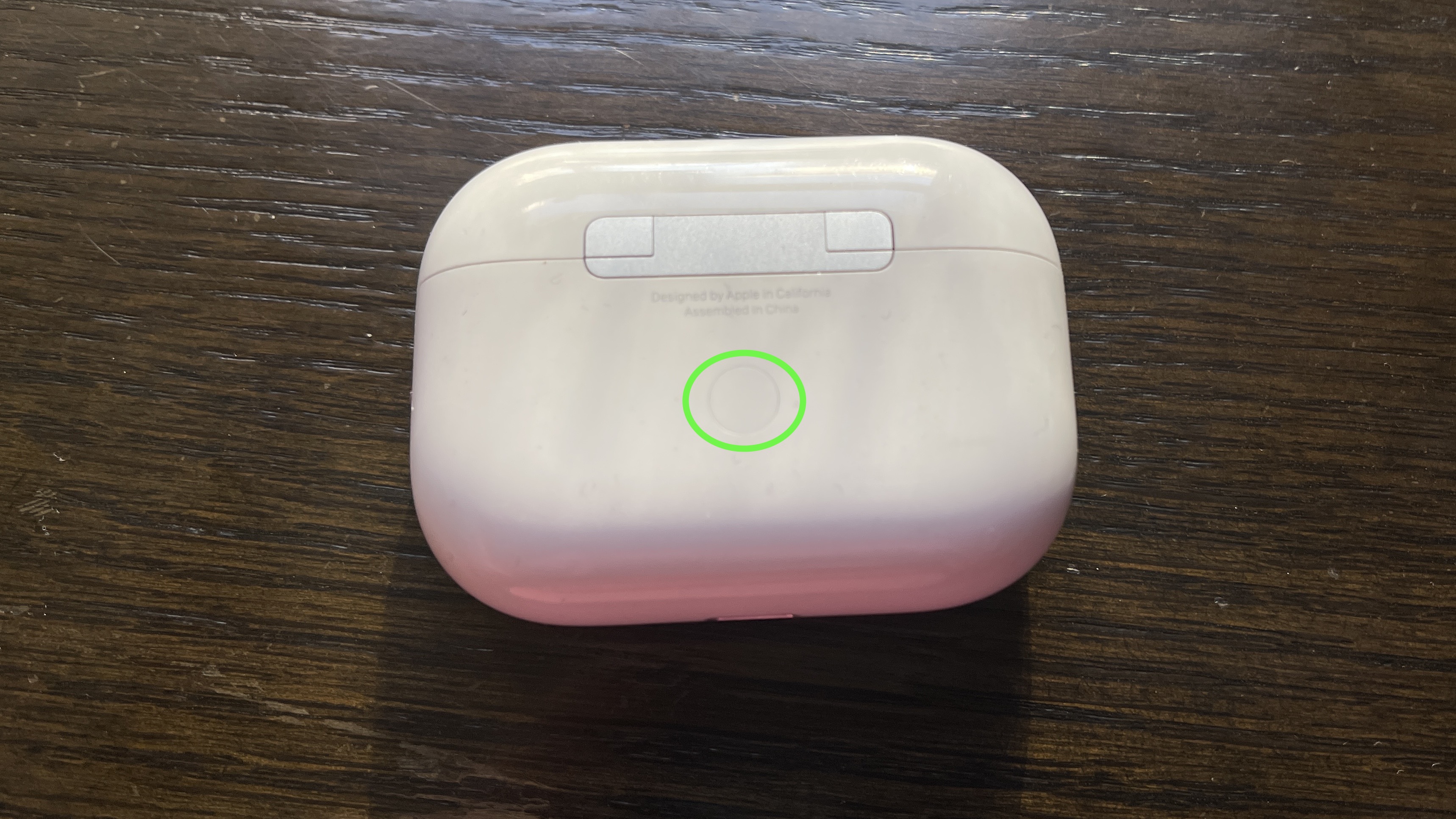 A green circle highlights the button on the back of the AirPods case