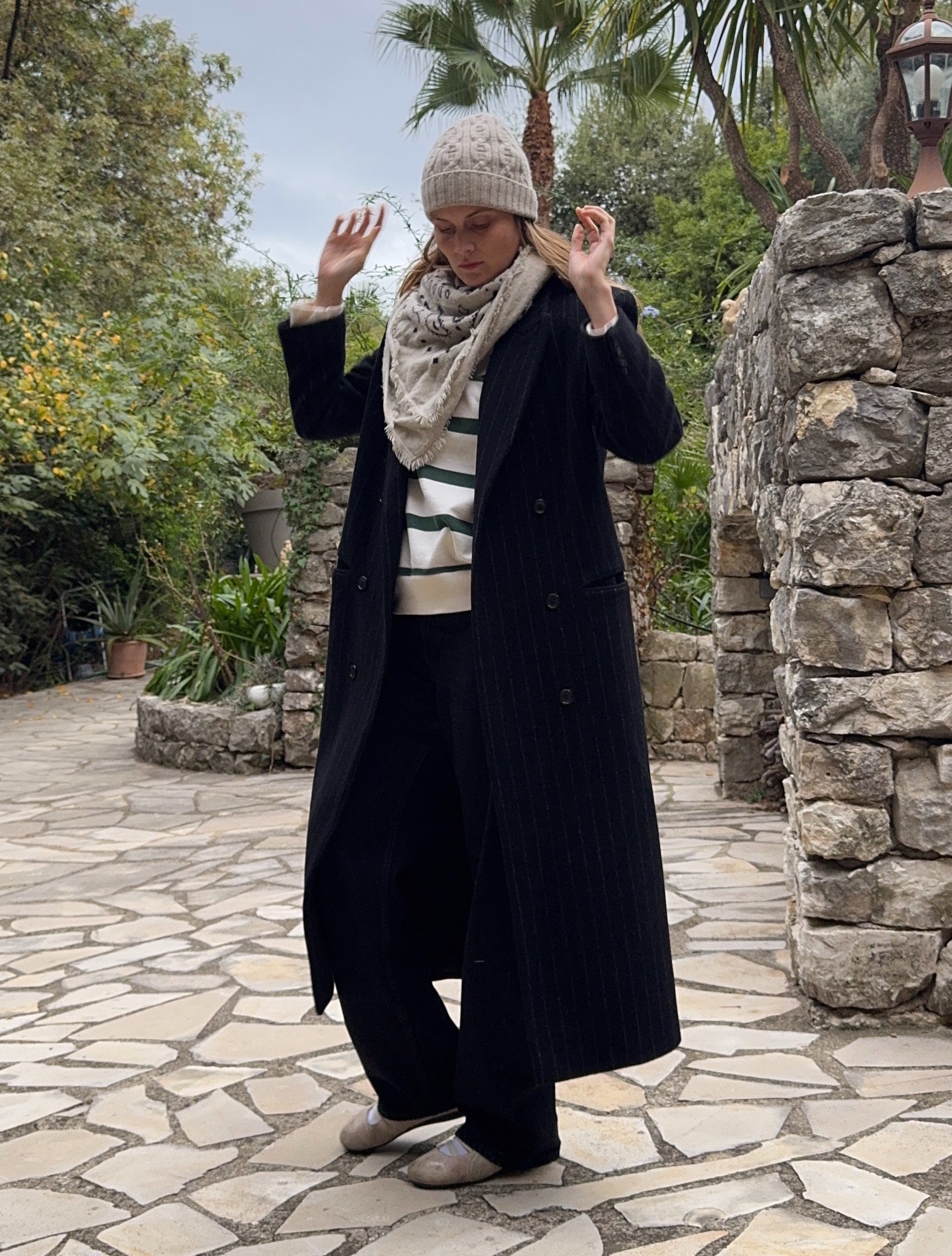 French writer and editor Eug&amp;eacute;nie Trochu poses in a beanie, scarf, long black coat, striped sweater, black pants, and Puma sneakers