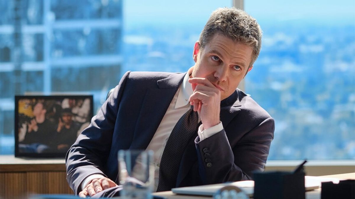 Attorney Ted Black (Stephen Amell) looks on thoughtfully as he sits in his sunny LA office decked out in a smart suit and tie in Suits LA.