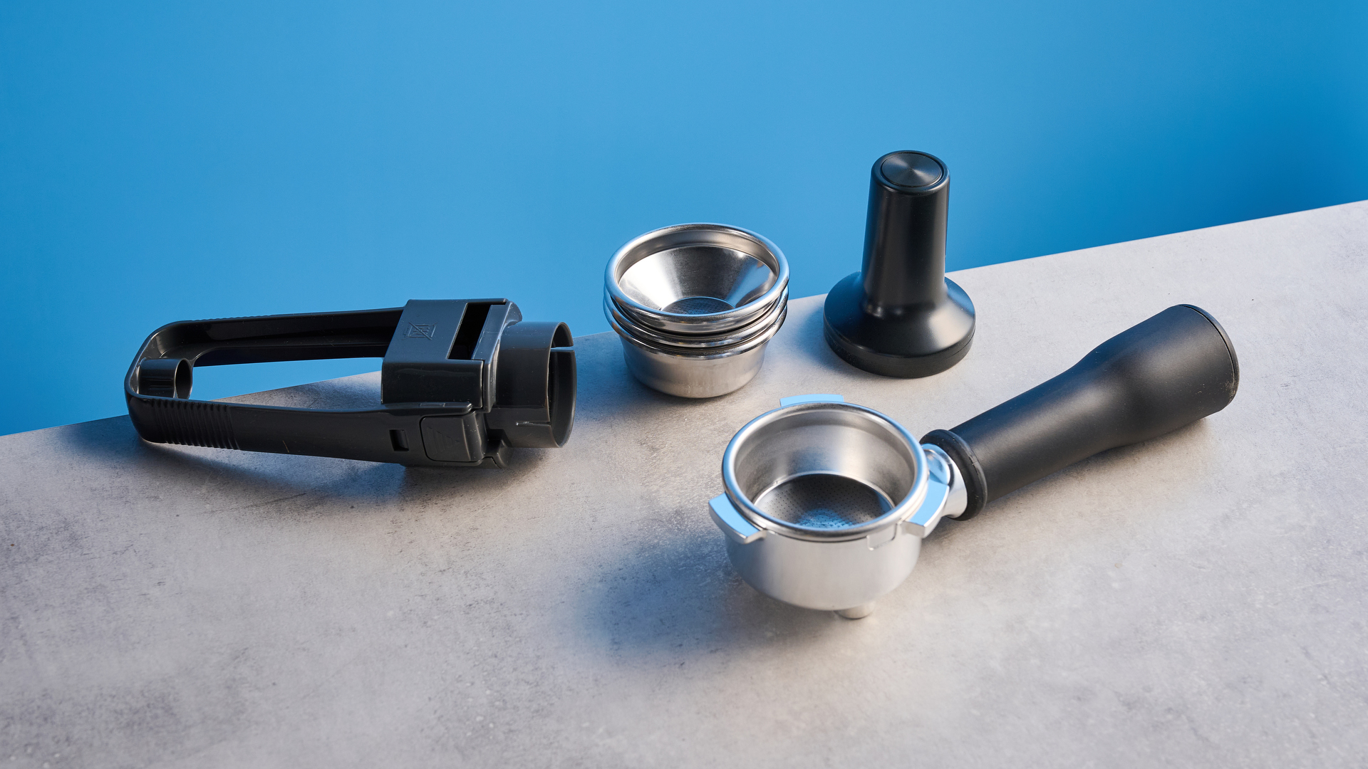 the breville bambino / sage bambino in silver photographed against a blue background with a wooden feature wall, showing the steam wand, group head, water tank, button controls, and espresso