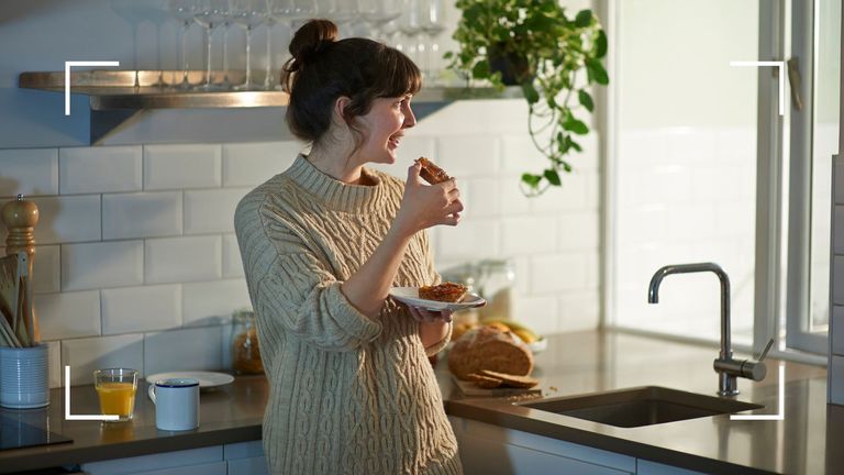 Woman eating breakfast of toast and jam, looking out of window in kitchen after learning how to lose a stone in a month