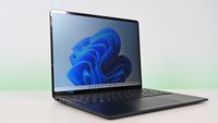 Suface Laptop for Business 8th Edition with a black keyboard and a modern design, displaying a blue abstract swirl on its screen, set against a light gradient background.