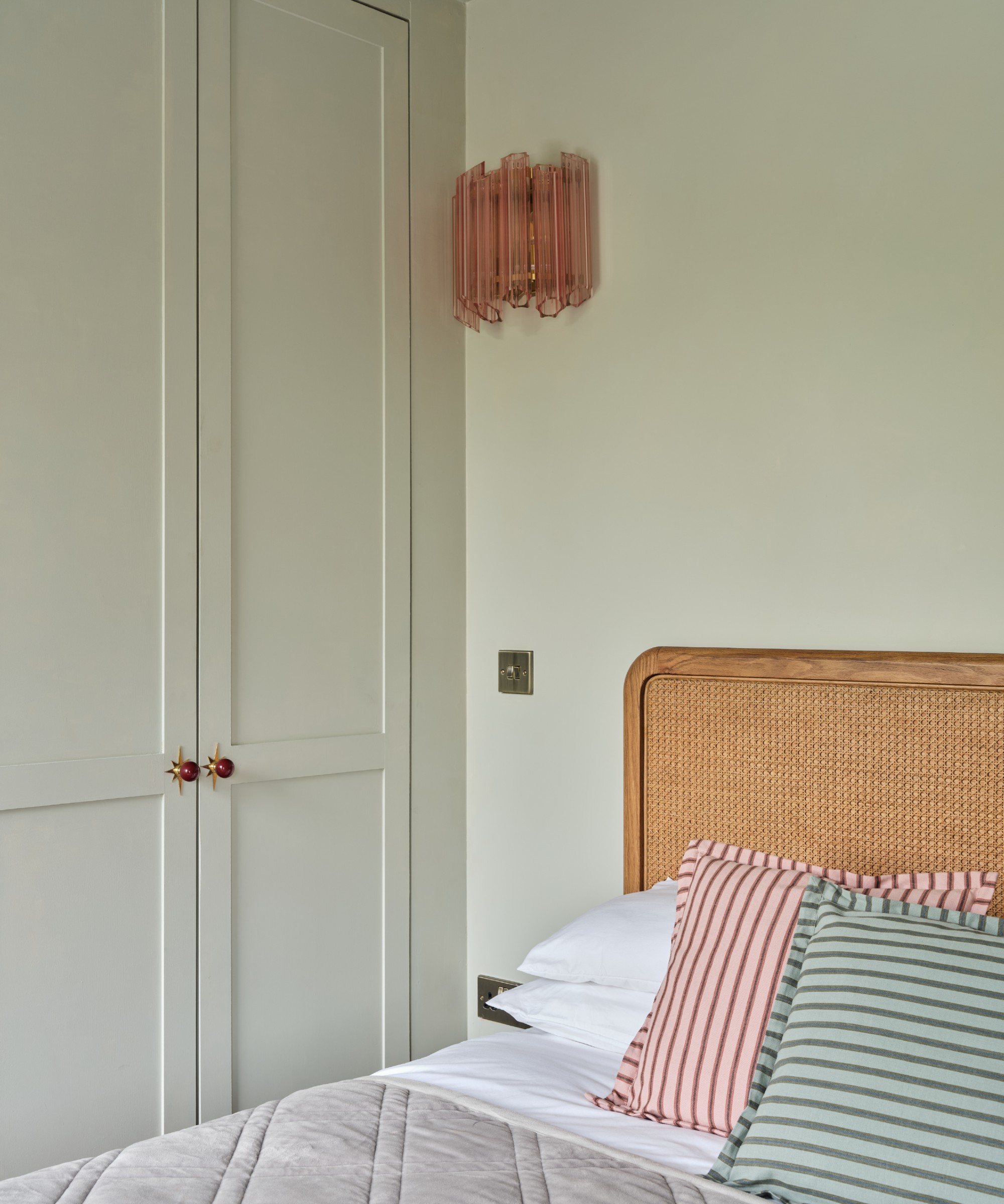 A bedroom painted in the lightest green shade with matching built-in wardrobes and a rattan headboard