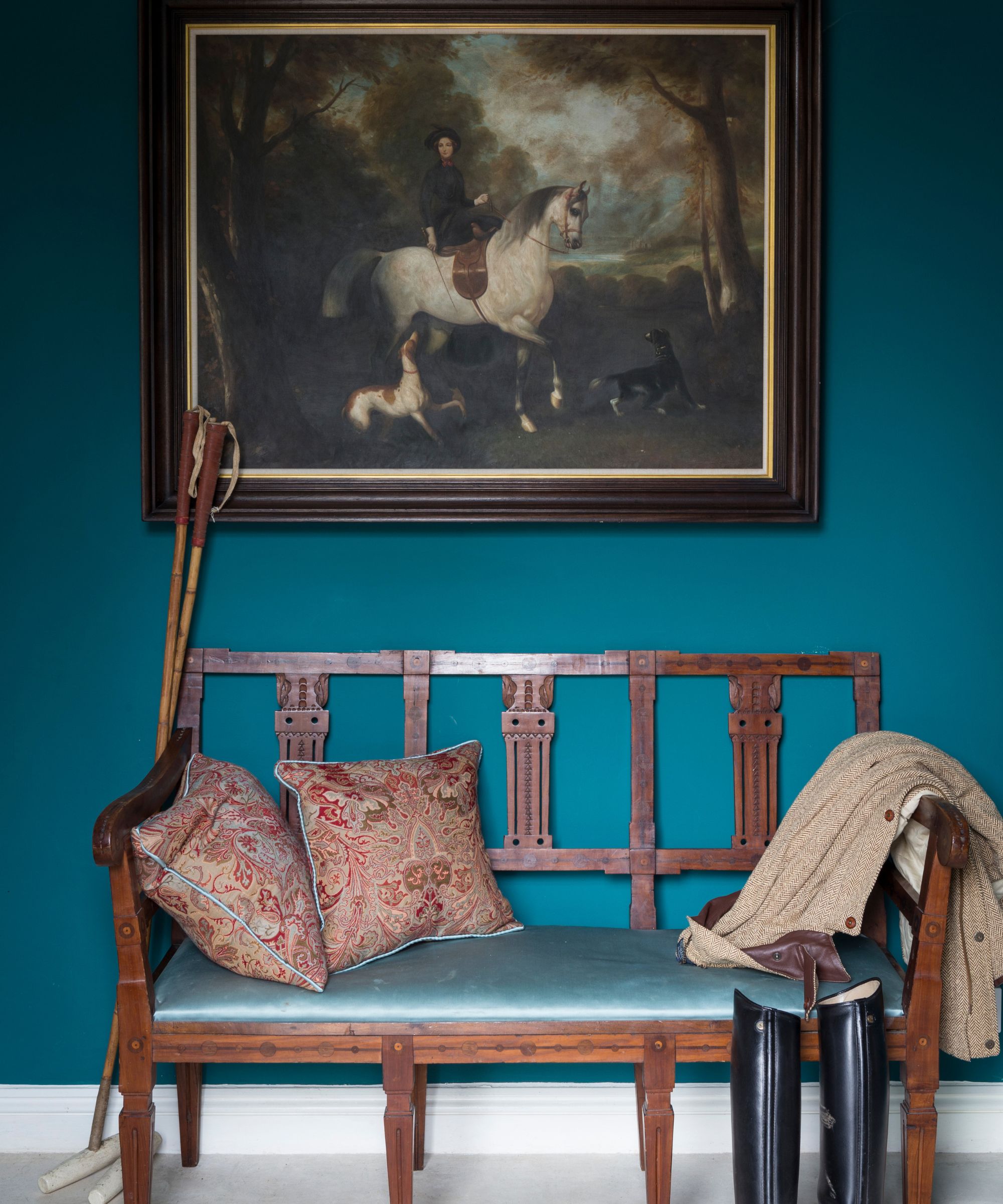 Hallway with bright blue wall, equestrian painting, wood antique bench, riding boots and silk cushions