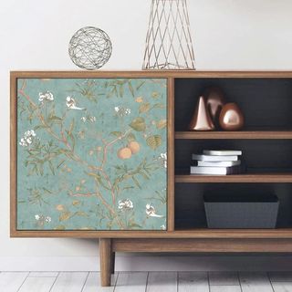 A cabinet on a wooden floor, where the door has been decorated with adhesive wallpaper