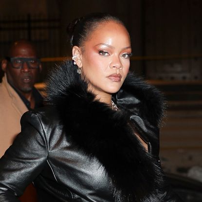 Rihanna is seen on February 13, 2026 in New York City wearing a fur-trimmed leather trench coat, lace underwear, sheer tights, and pointed-toe pumps