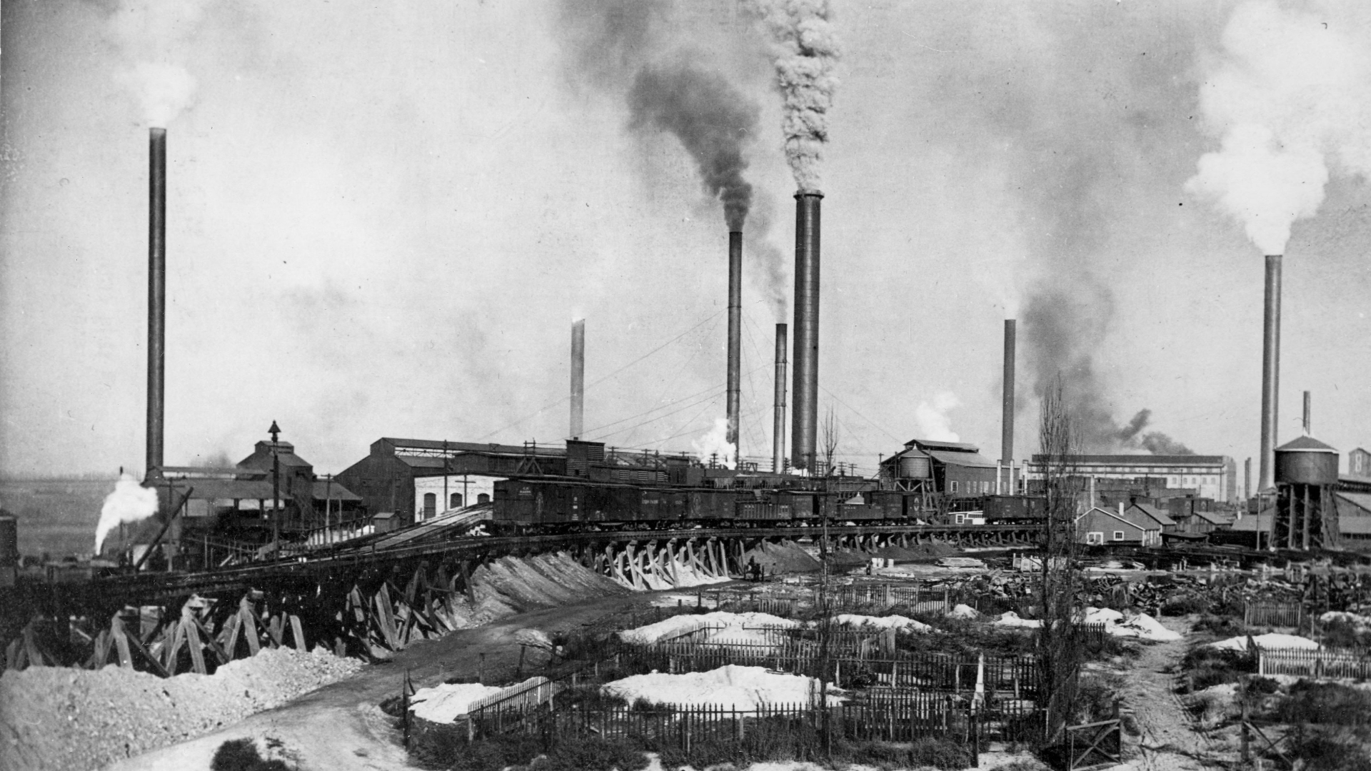 black-and-white photo of a smelting plant with smoke stacks belching smoke