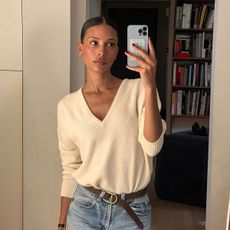 A woman in a chic, cream V-neck jumper, taking a mirror selfie