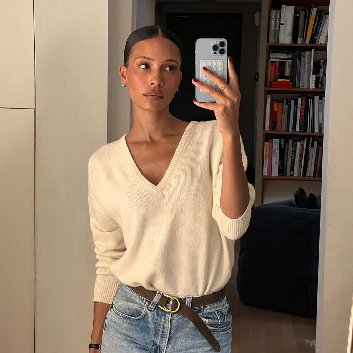 A woman in a chic, cream V-neck jumper, taking a mirror selfie