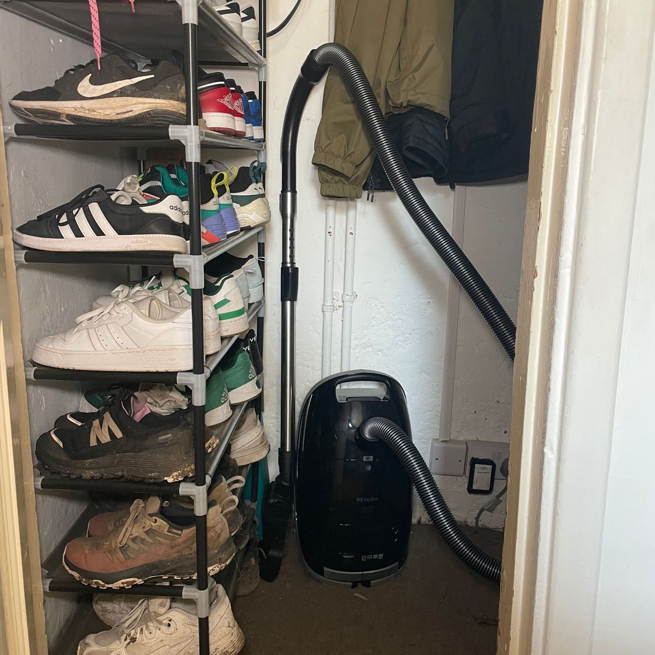 Miele M1 Guard cylinder vacuum cleaner stored in an under-the-stairs cupboard next to a shoe rack