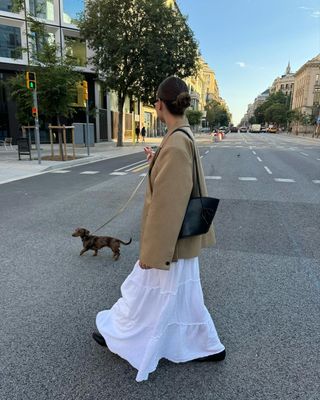 @manondevelder walking dog across the street wearing baggy brown blazer and white maxi skirt