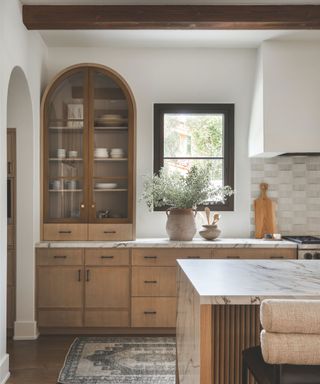 wooden cabinetry in kitchen with marble countertops and arched storage unit