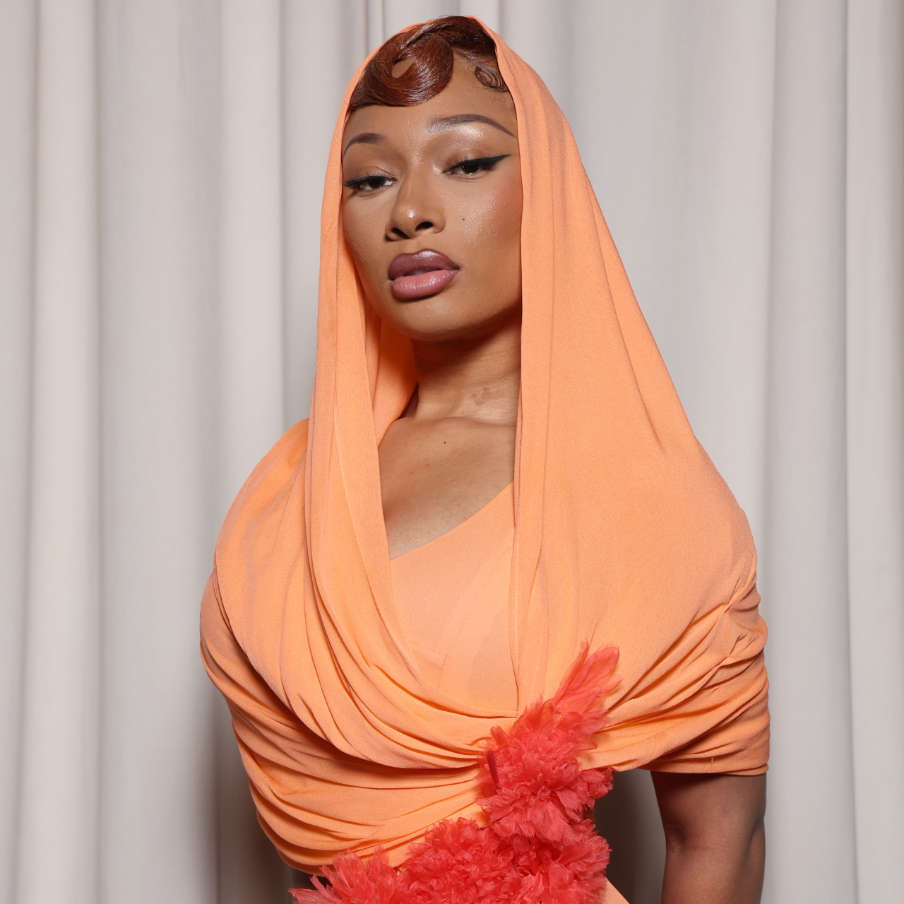 Megan Thee Stallion wearing a hooded dress and winged eyeliner.