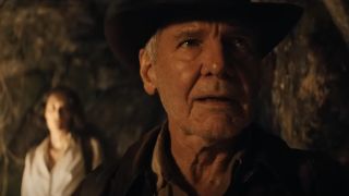 Harrison Ford smiling as he explores a cave with Phoebe Waller-Bridge behind him in Indiana Jones and the Dial of Destiny.