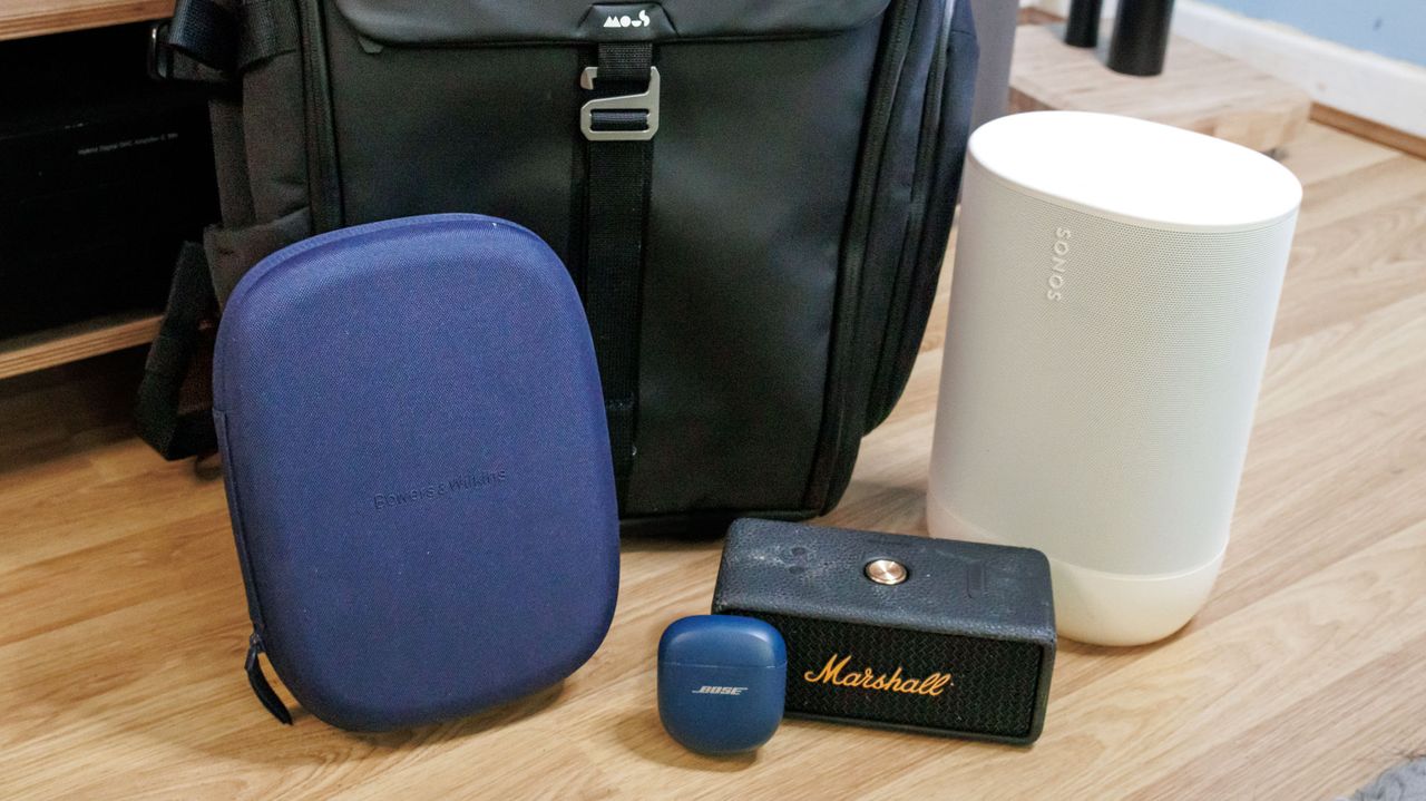 Mous Protective Lid backpack with a pair of Bowers &amp; Wilkins Px7 S3, Bose QuietComfort Ultra Earbuds, Marshall Emberton III, and Sonos Move 2 in front of a stereo system