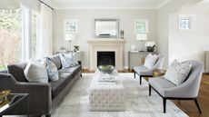 A neutral living room with white fireplace, gray sofa, and tall windows