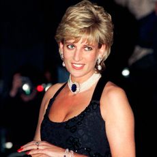 Princess Diana wearing a black dress and pearl necklace smiling at a 1995 charity gala