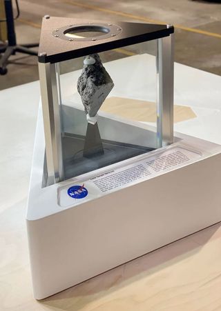 a gray rock is displayed under glass on a white base