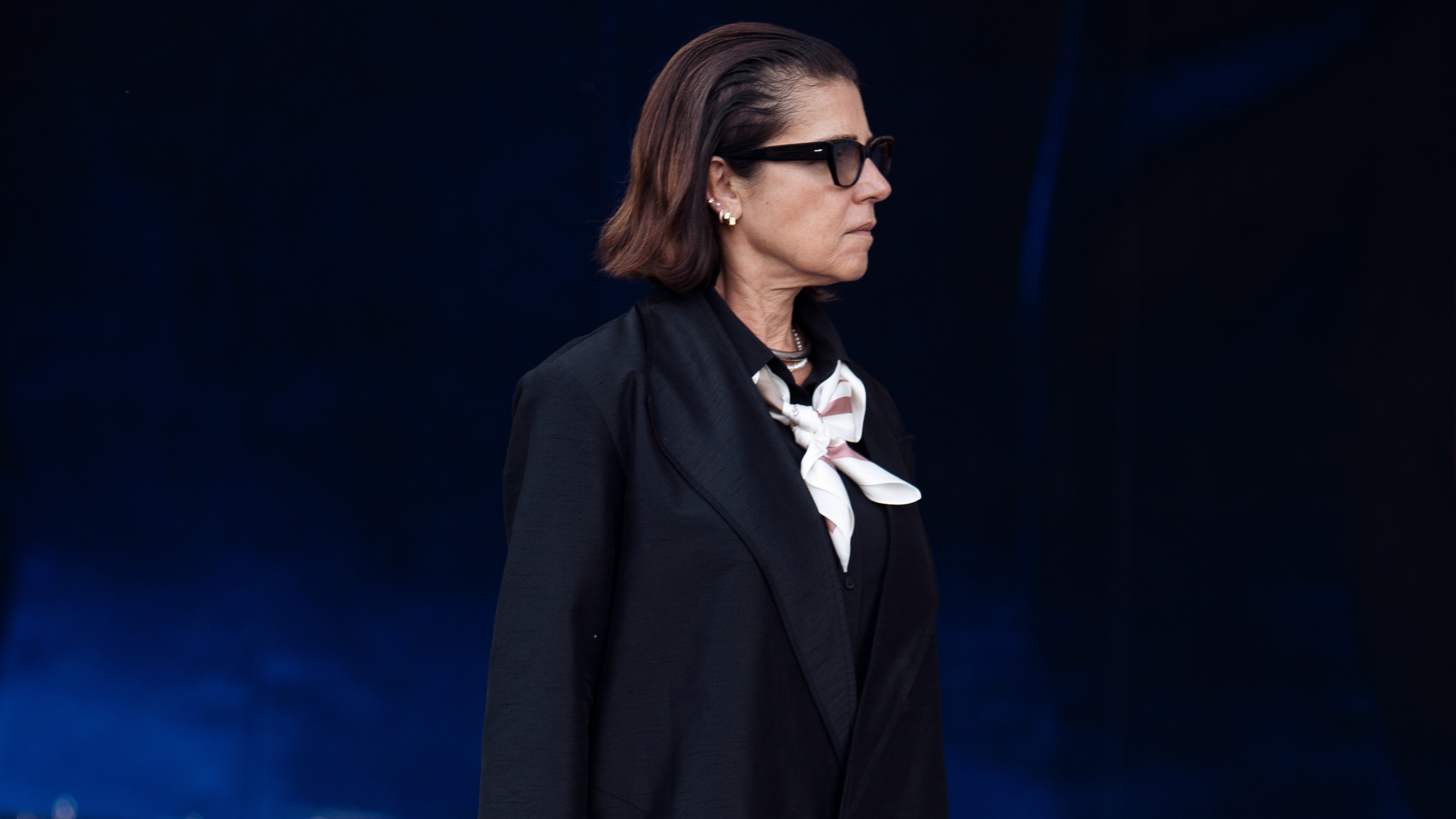 Woman wearing black jacket, black platform sneakers, and black trousers in street style photo.