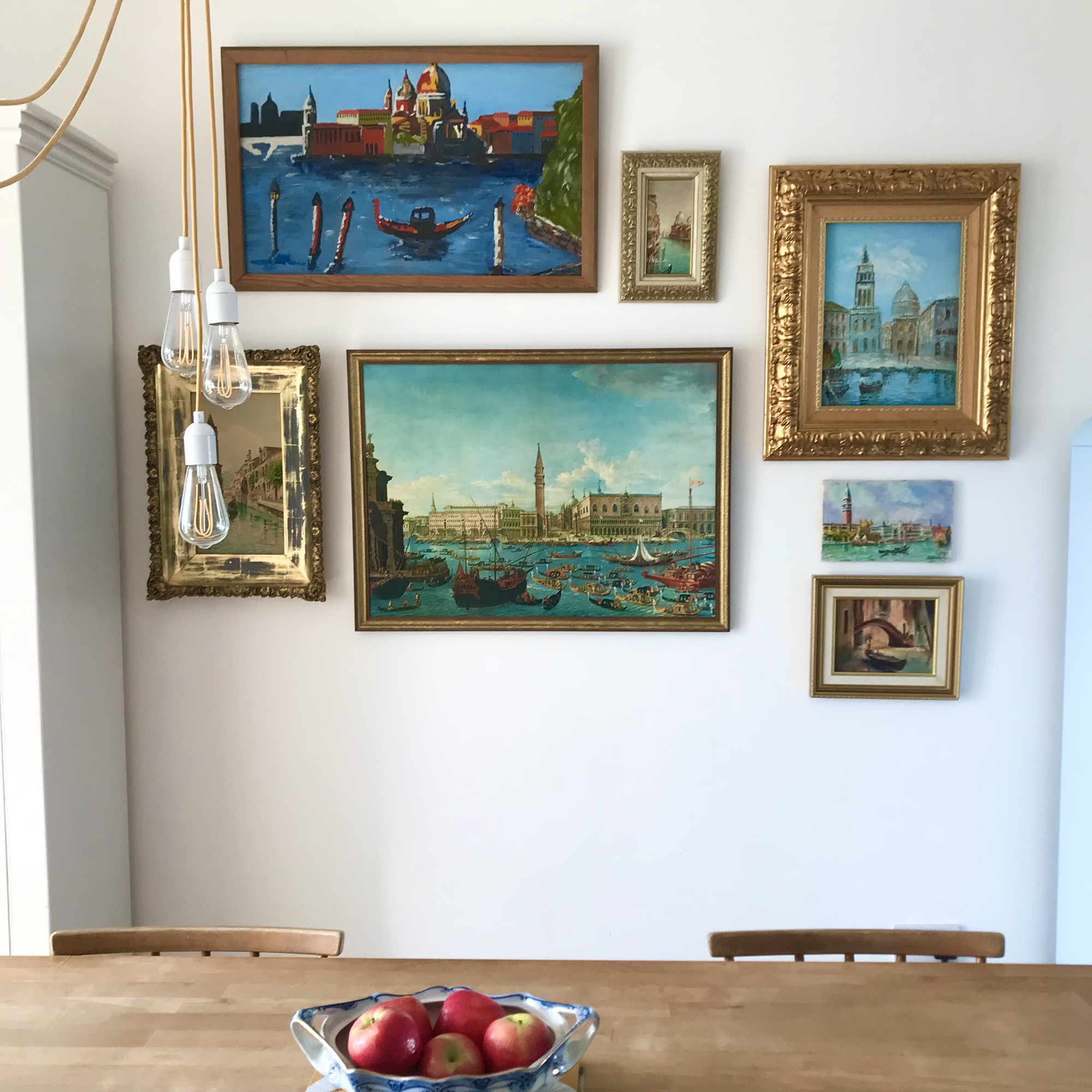 White dining room with vintage paintings in gold frames arranged to form a gallery wall