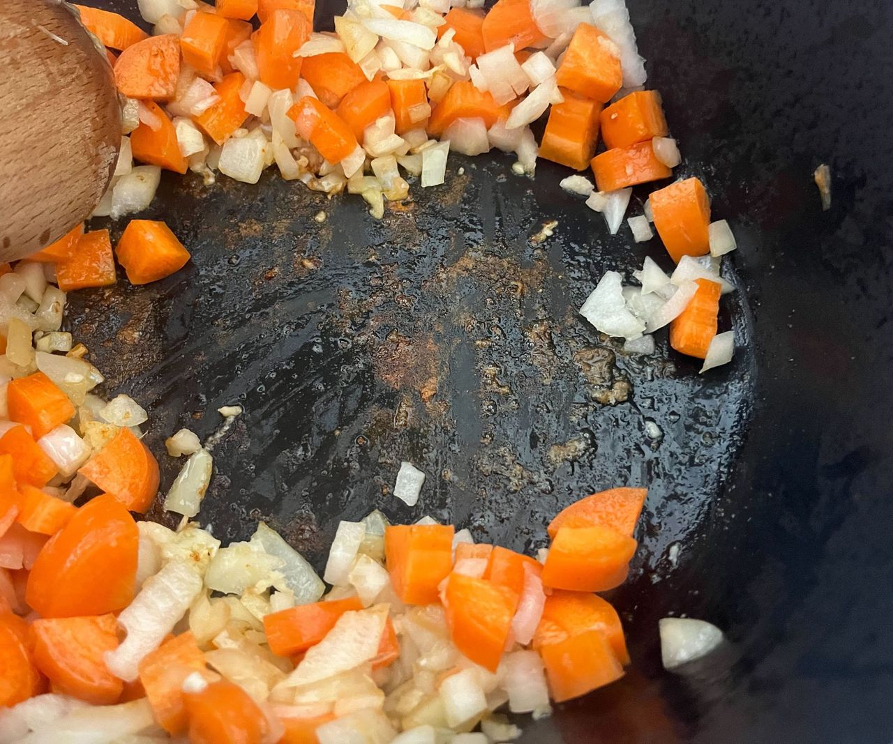 The fond on the base of a black Dutch oven filled with carrots and onions