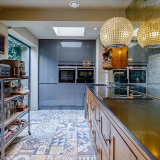 Stylish kitchen with wooden cupboards with built-in hob and basin with tap next to eye-level appliances with a beautiful tiled floor with a mix of patterns and colours