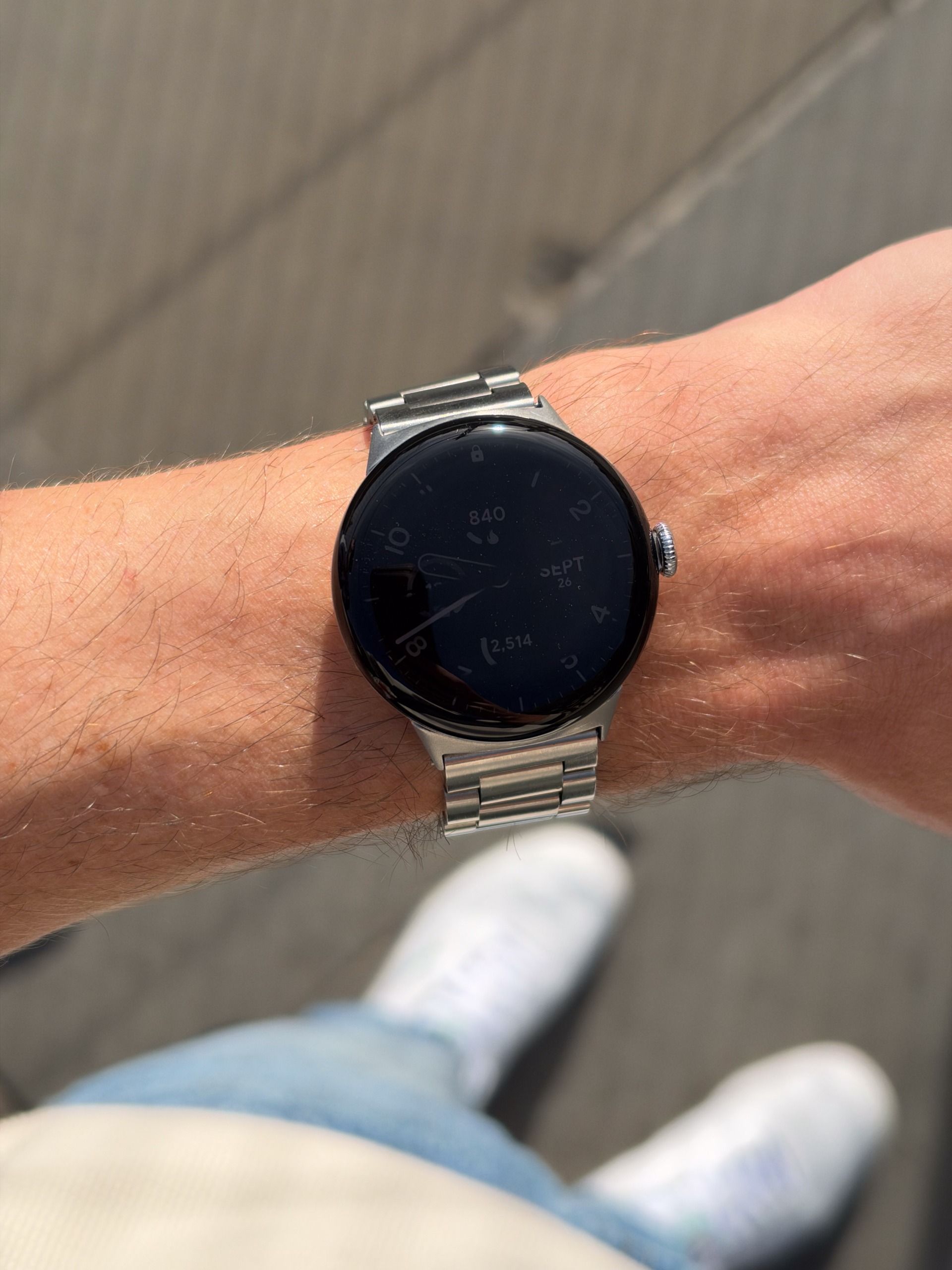 Round smartwatch with a silver metal bracelet worn on a wrist in bright sunlight.