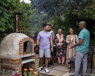 Family members in a garden gathered round a pizza oven