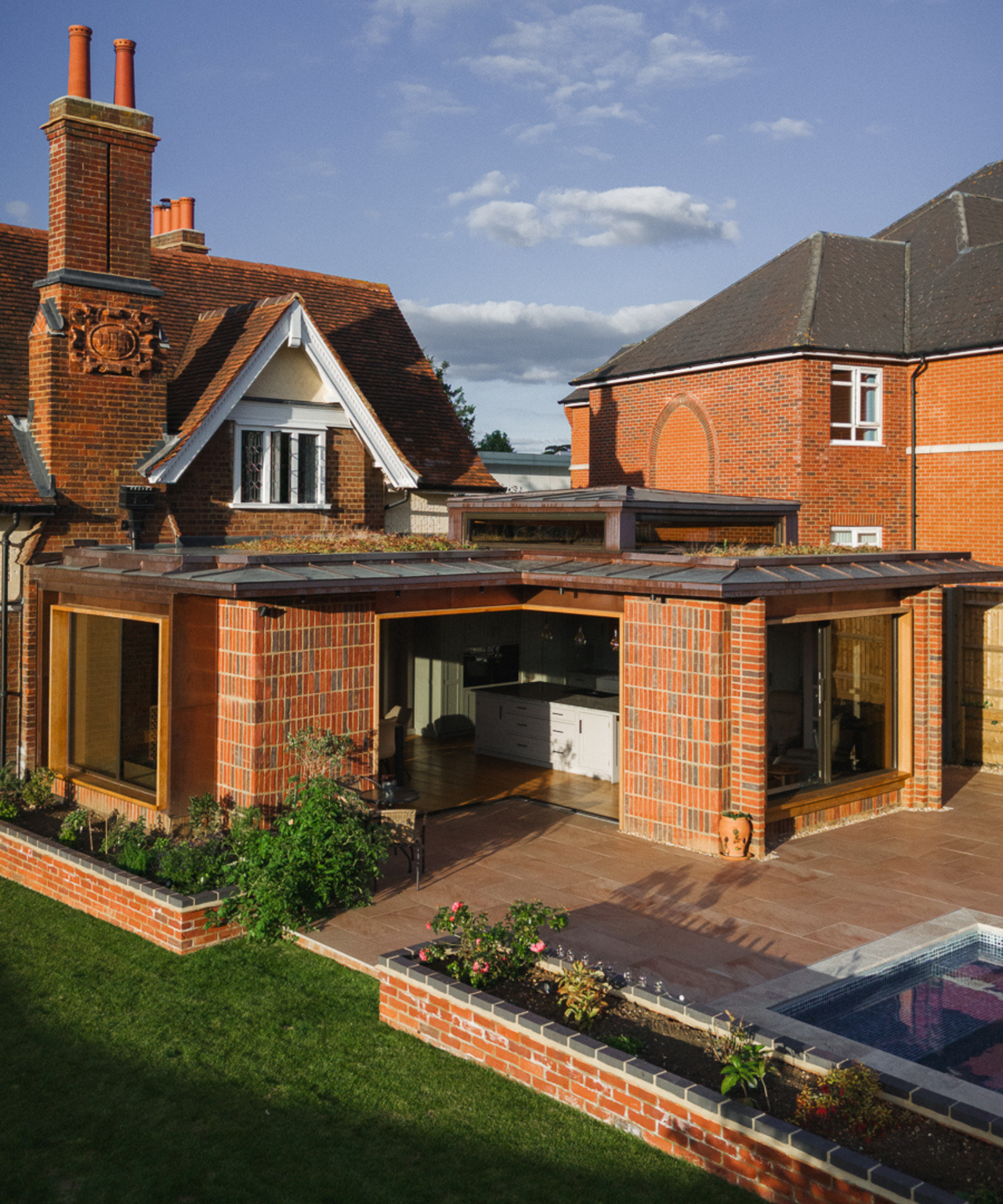 Red brick house with L-shaped kitchen extension leading onto patio with pool