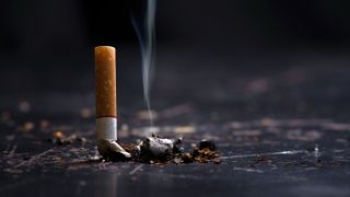 A cigarette butt with smoke emanating from it.