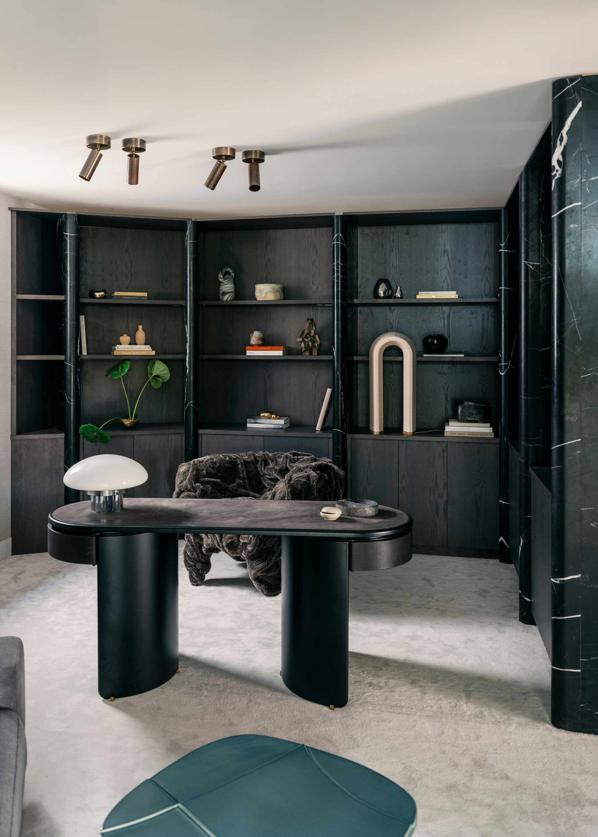 a home offie with black wall to wall storage units with marble pillar details in between each section; a black wooden solid statement desk and neutral carpet and ceiling