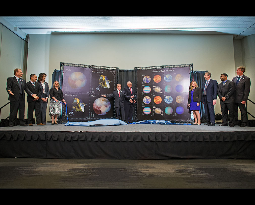 Researchers and USPS officials pose with stamp photos, formerly-covering curtains on the ground