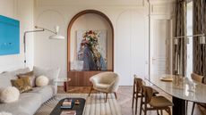 Image of a formal living room with a beige color scheme and a pop of blue. There is a modern gray sofa and a beige rug underneath. A boucle chair is in front of a sofa. The room also has a marble dining table with four chairs around it.