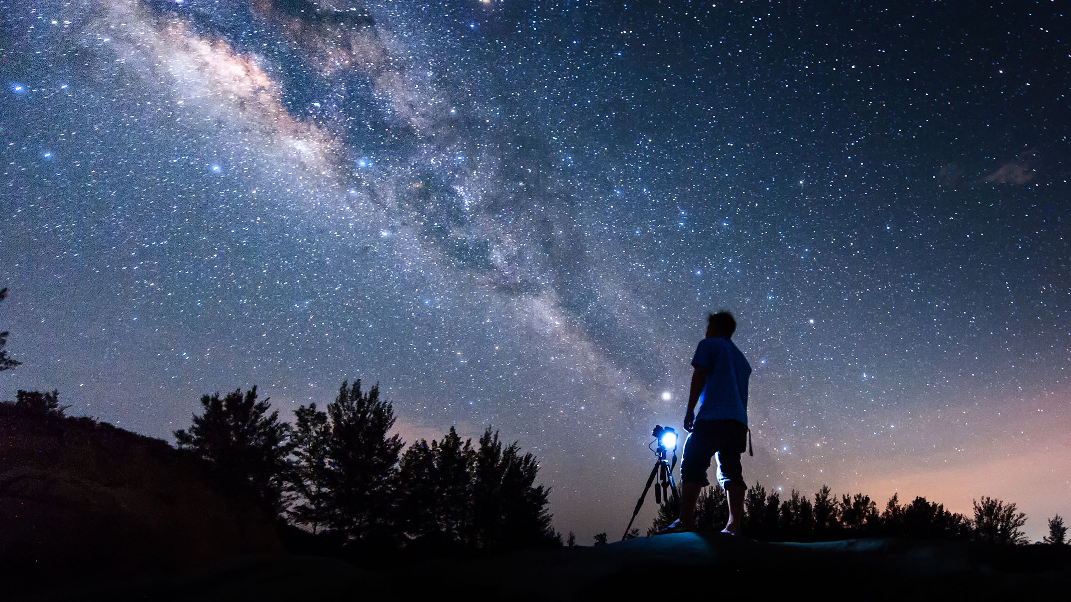 Photographer using camera on tripod under night sky