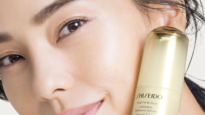 woman holding shiseido LiftDefine Radiance Serum to her face with glowing, smooth skin