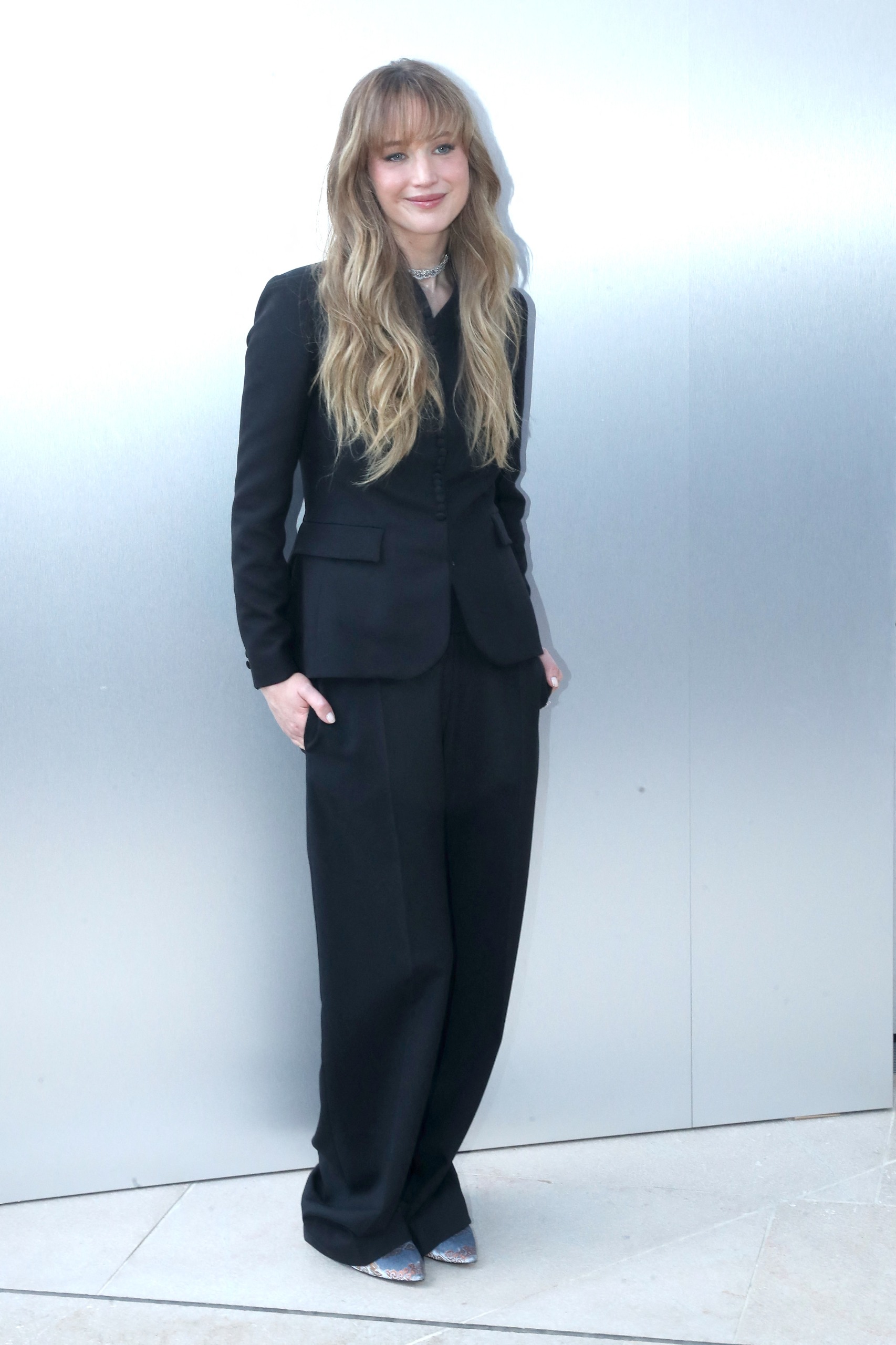 Jennifer Lawrence has long blonde hair and is wearing a black Dior suit, Priyanka Chopra wears her black hair tied back and wears a black Dior dress with a white tiered skirt