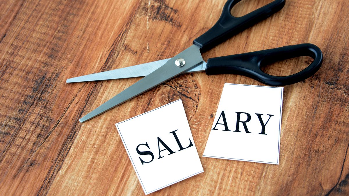 A card with the word salary on it that&amp;#039;s been cut in half lying on a table with a pair of scissors