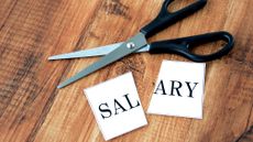 A card with the word salary on it that's been cut in half lying on a table with a pair of scissors